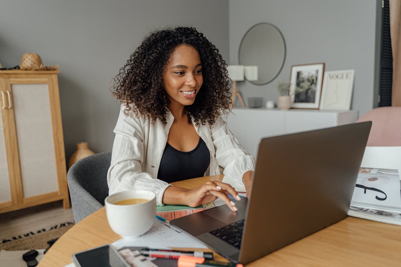 programs-02 A woman sits at a round table, working on a laptop with a coffee cup nearby in a cozy home office setting.